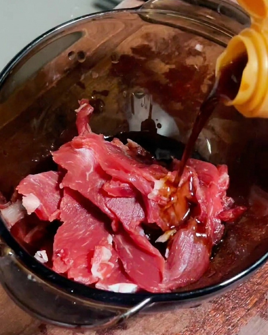 Salsa de soja vertiéndose sobre tiras de carne cruda en un bol de cristal.