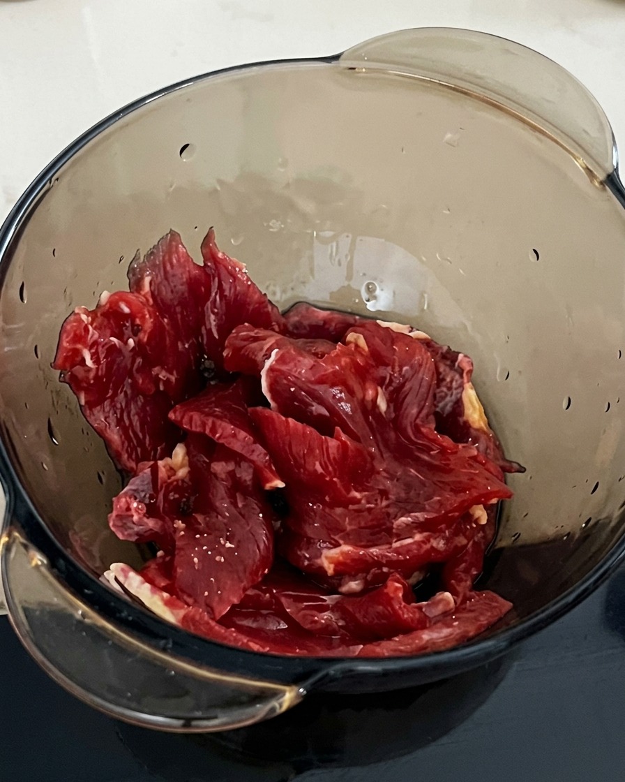 Una cucharada de almidón siendo añadida a un bol con tiras de ternera y salsa de soja.