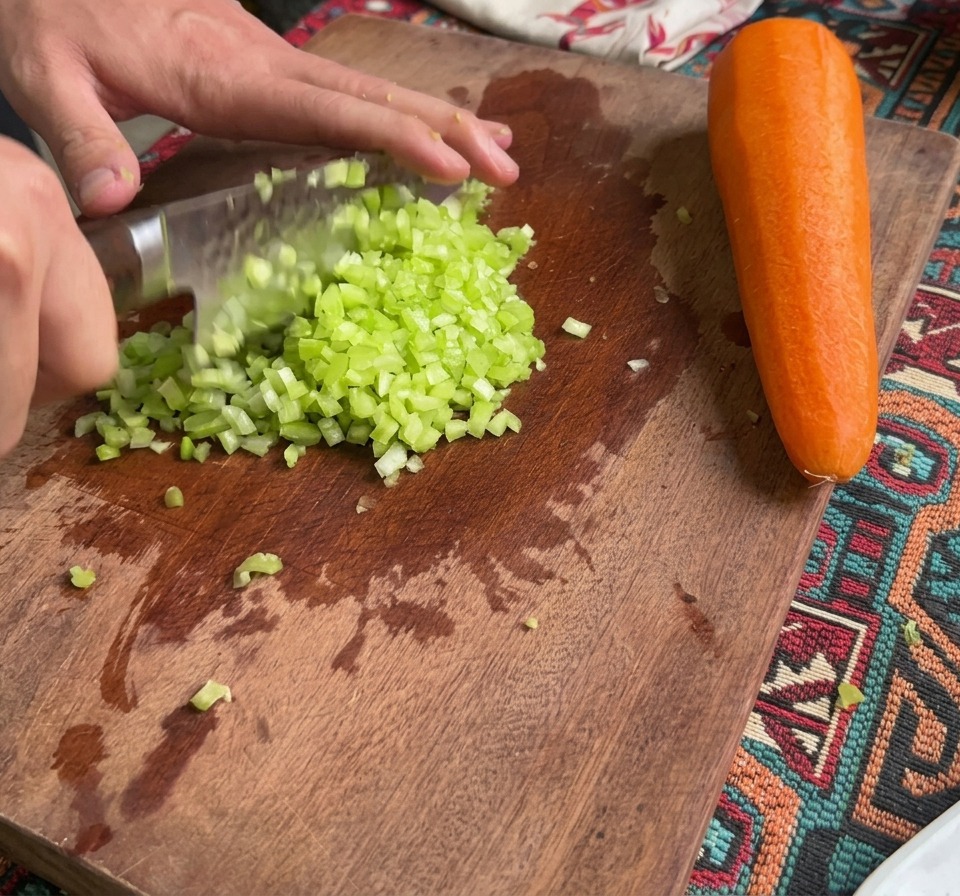 Apio y zanahorias finamente picados sobre una tabla de cortar de madera junto a una zanahoria entera.