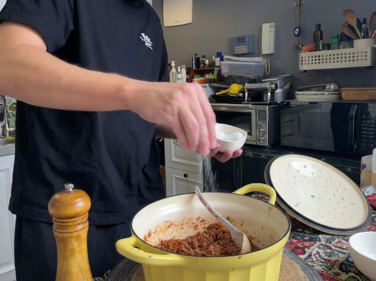 Pimienta negra recién molida y sal siendo añadidas a una olla de ragú de carne terminado.