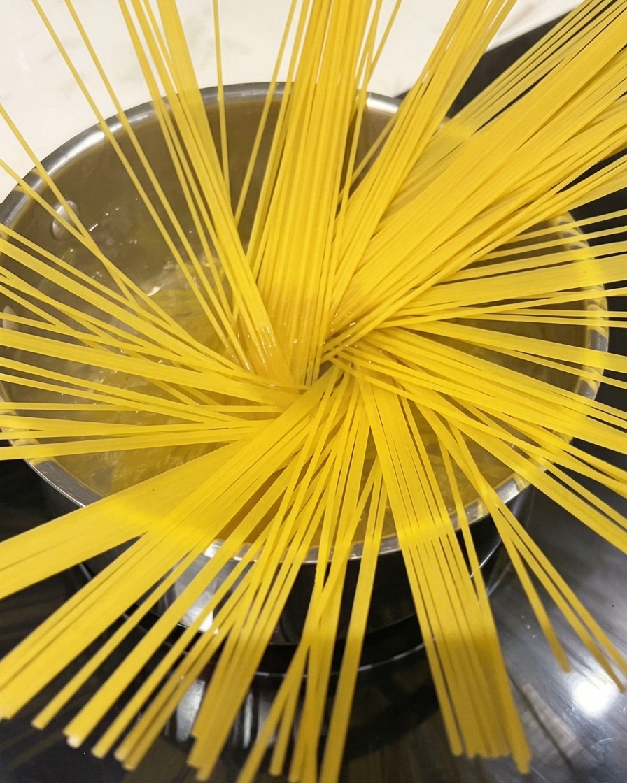 Fideos de espagueti hirviendo en una olla grande con agua, con vapor saliendo.