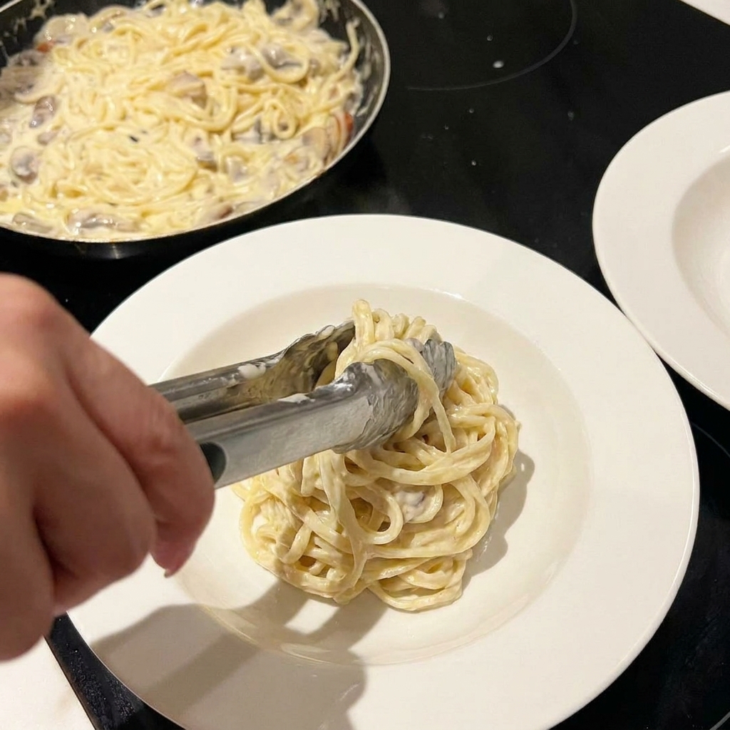 Pasta cremosa siendo mezclada en la sartén con queso y especias espolvoreadas por encima.