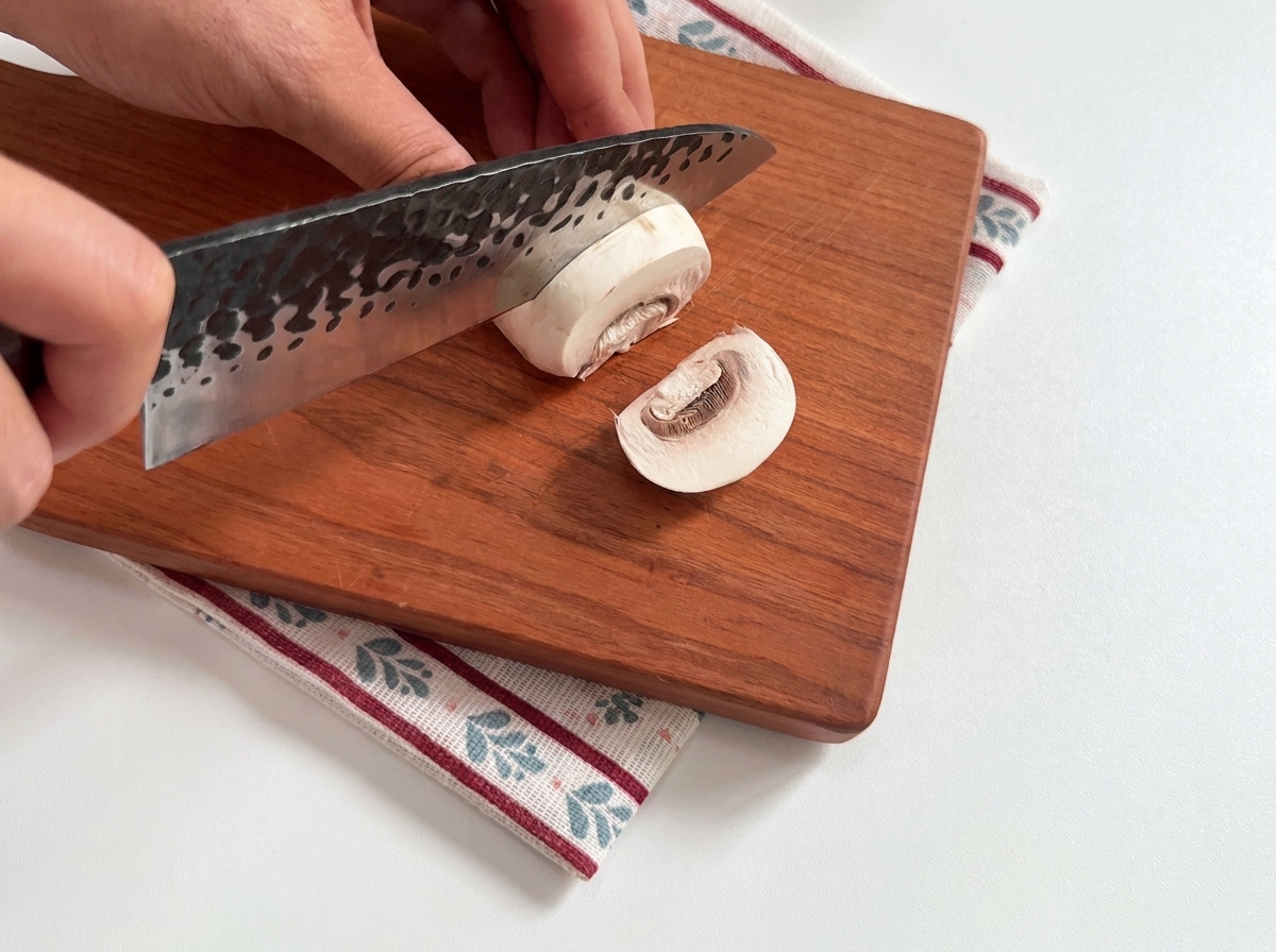 Champiñones blancos frescos siendo rebanados sobre una tabla.