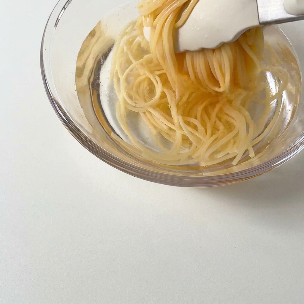 Espaguetis cocidos siendo colocados en un cuenco con agua fría.