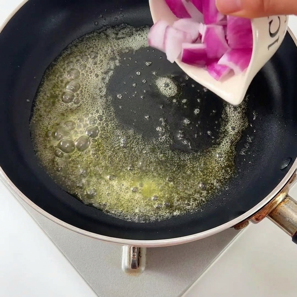 Cebolla picada vertiéndose en una sartén con mantequilla.
