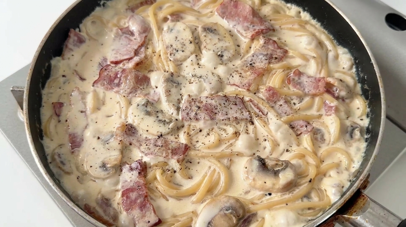 Espaguetis cremosos con champiñones y tocino recién preparados, cubiertos con una rica salsa y pimienta negra recién molida.