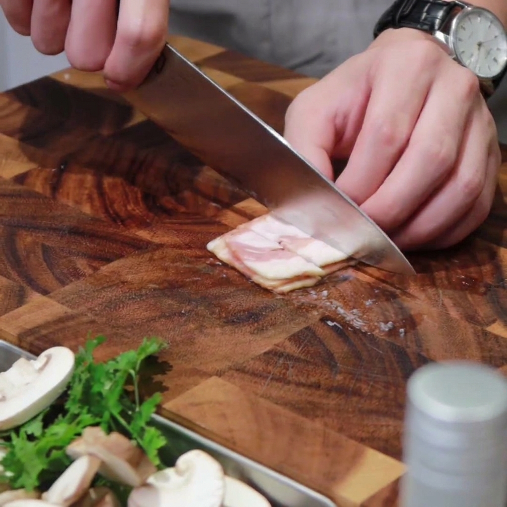 Tiras de bacon cortándose en trozos pequeños sobre una tabla de madera.