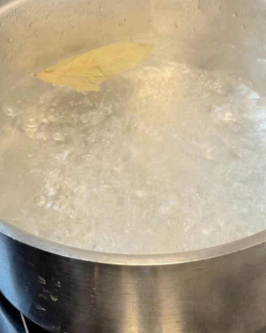 Pasta cocinándose en una olla de agua hirviendo con dos hojas de laurel flotando en la superficie.