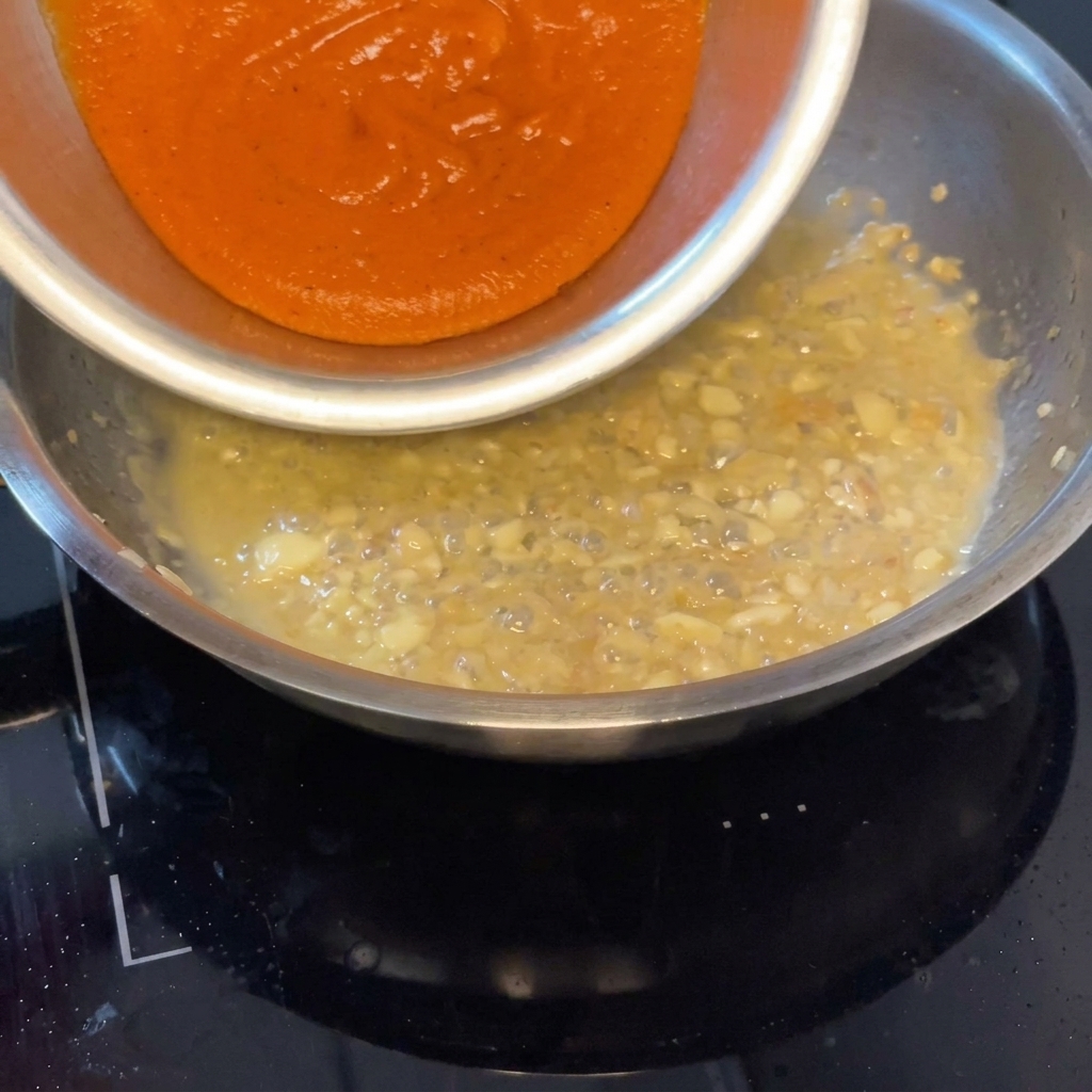 Salsa de pimientos asados siendo vertida en la sartén para mezclarse con el líquido aromático.