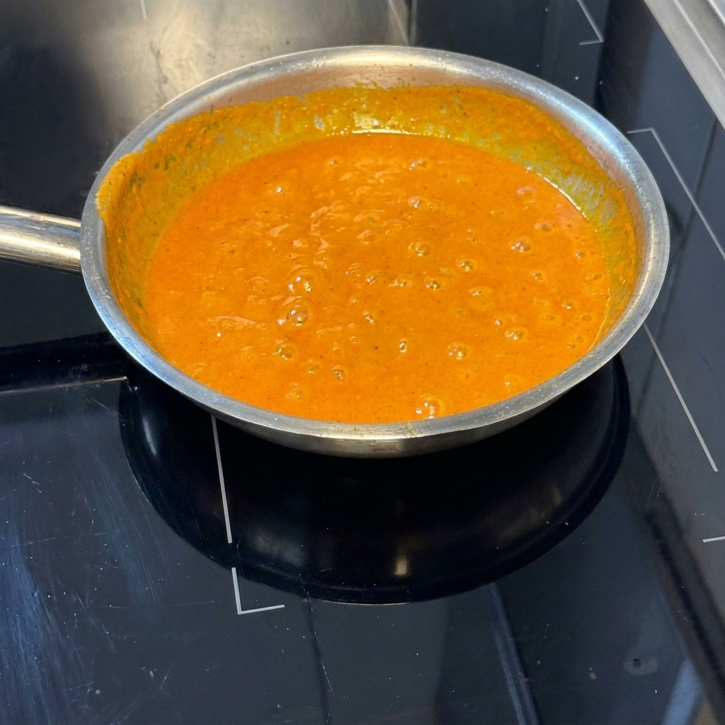 Hebras de pasta cocida siendo mezcladas con la vibrante salsa de pimientos asados en la sartén.