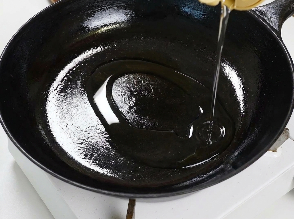 Ajo en láminas y copos de chile rojo chisporroteando en aceite en una sartén plana, removidos con una espátula de madera.