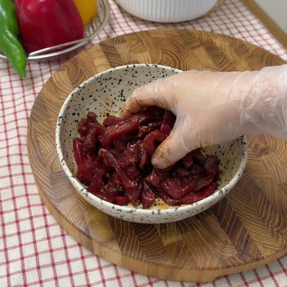 Tiras de ternera cruda marinándose en un cuenco moteado con salsa de soja y condimentos.