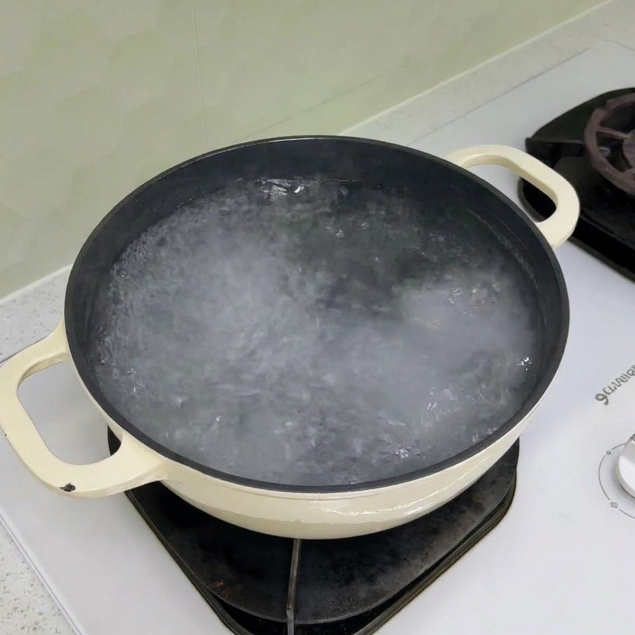 Pasta rotini seca añadiéndose a una olla con agua hirviendo.
