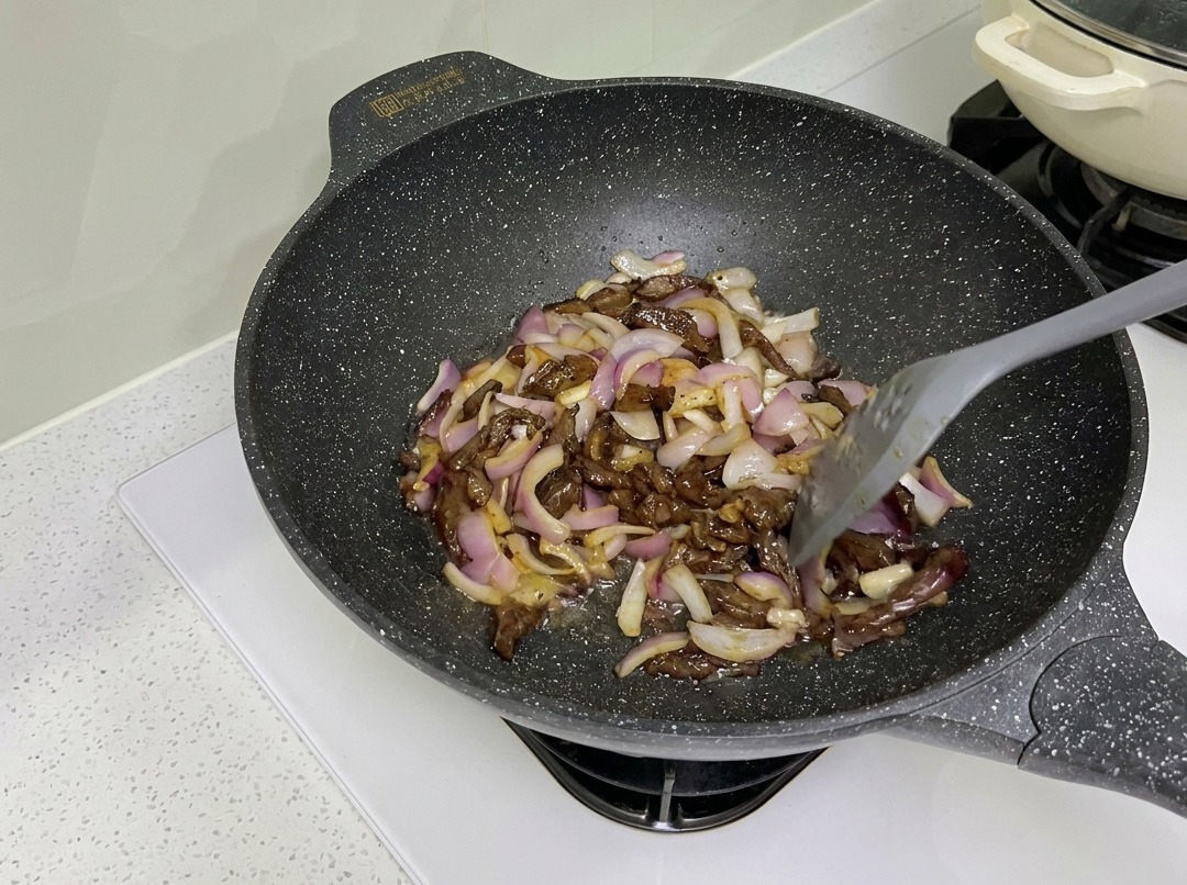 Tiras de ternera y cebolla morada salteándose juntas en un wok.