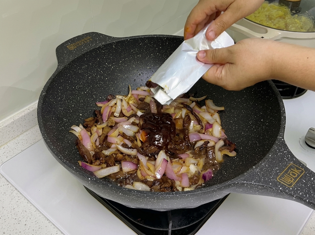 Salsa oscura y pasta de tomate mezclándose en un wok con tiras de ternera y cebolla morada salteada.