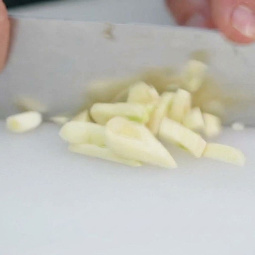 Dientes de ajo frescos siendo picados finamente sobre una tabla.