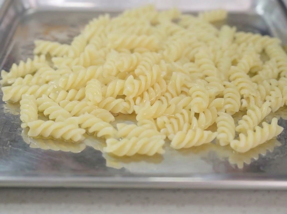 Pasta cocida reposando en una bandeja metálica con un chorrito de aceite de oliva por encima.