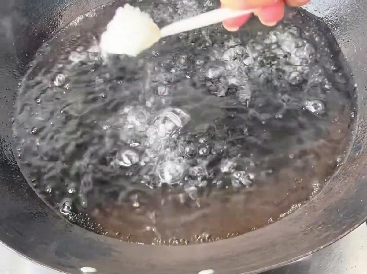 Una cucharada de sal blanca siendo añadida a un gran wok de hierro lleno de agua hirviendo.