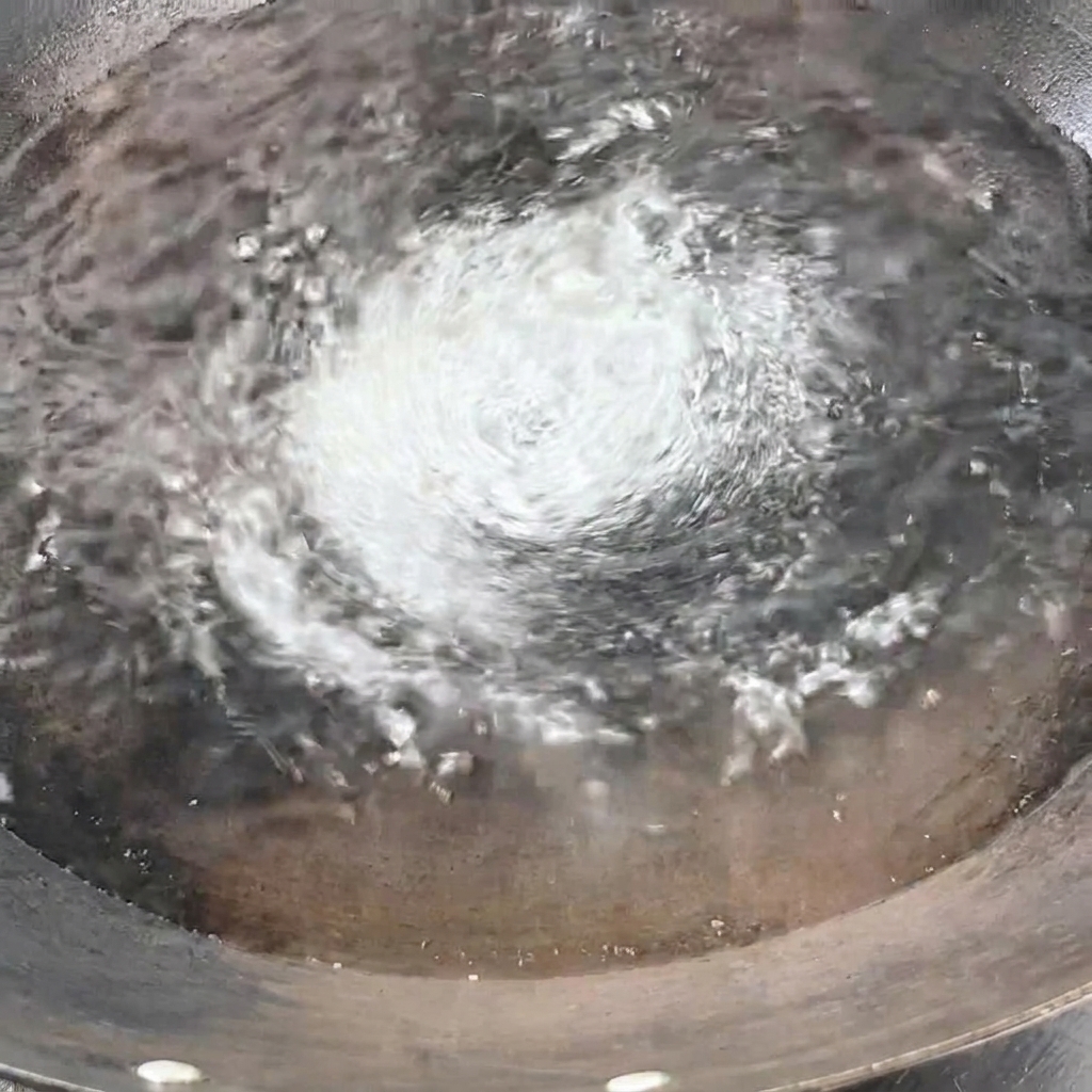 Un manojo de espaguetis secos siendo introducidos verticalmente en el agua hirviendo del wok.