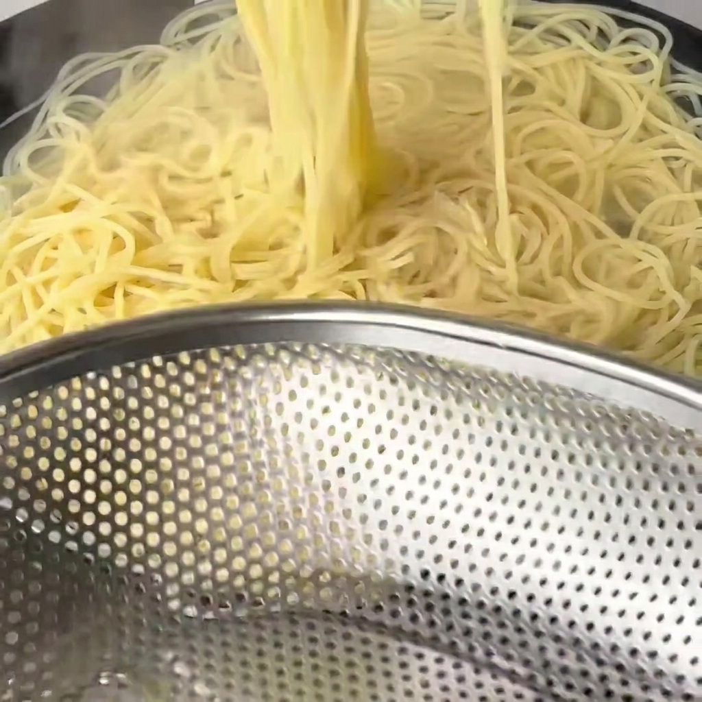 Fideos cocidos y blandos siendo retirados del agua con palillos de madera largos.