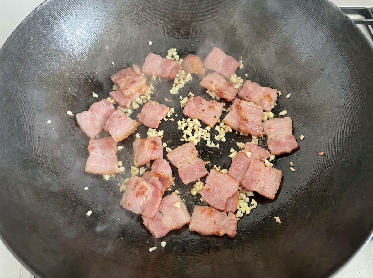 Champiñones blancos rebanados siendo vertidos en el wok con la mezcla de beicon y ajo.