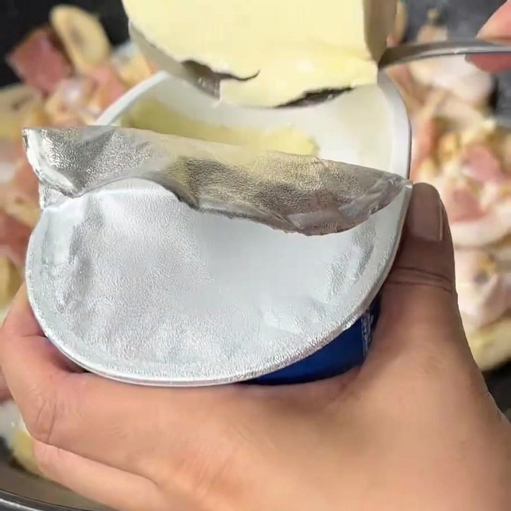 Queso crema siendo añadido a una salsa de leche y vegetales hirviendo en un wok.