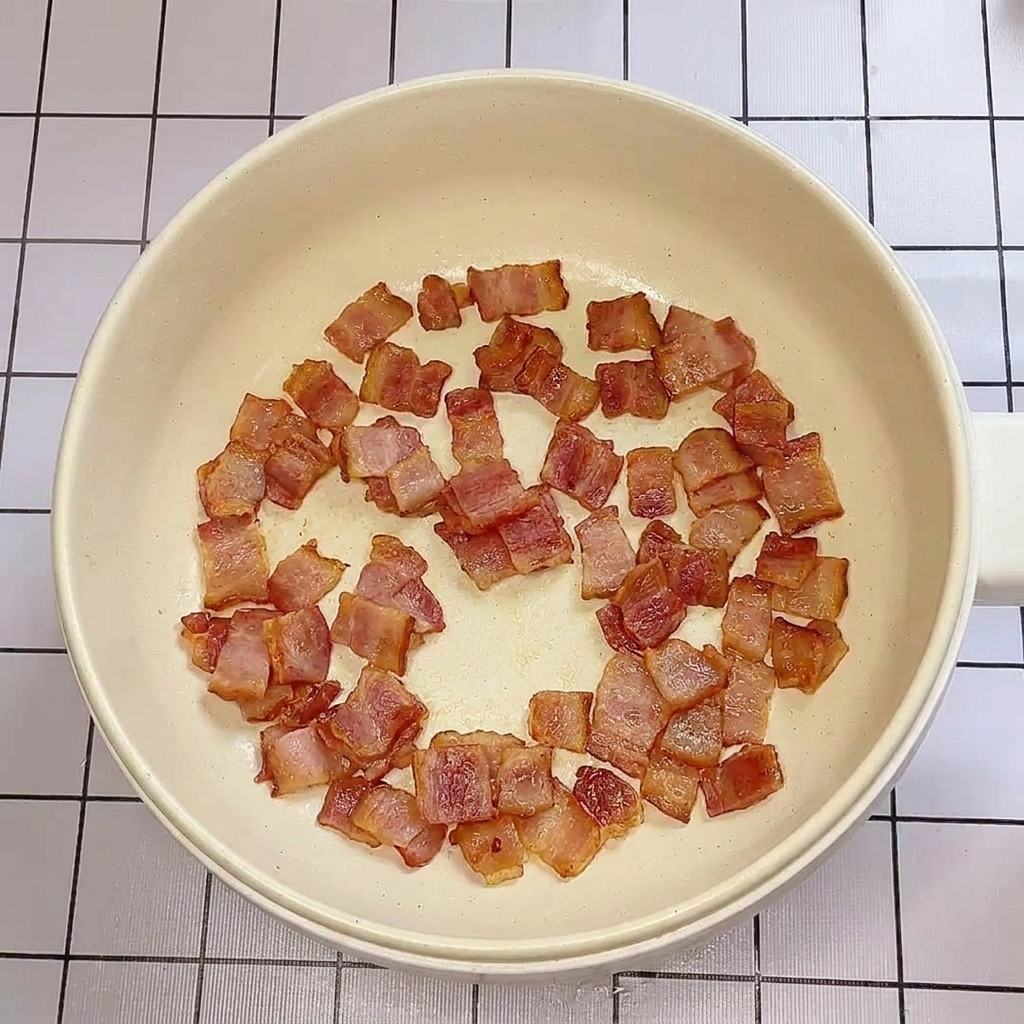 Trozos de tocino crujientes y dorados cocinándose en una sartén baja.
