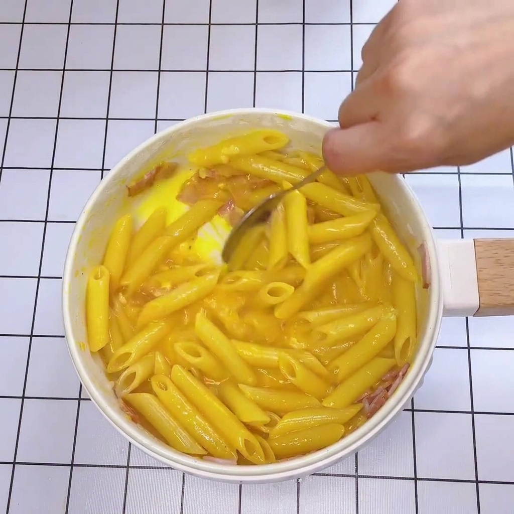 Primer plano de una cuchara mezclando rápidamente la pasta en la sartén con la salsa cremosa.