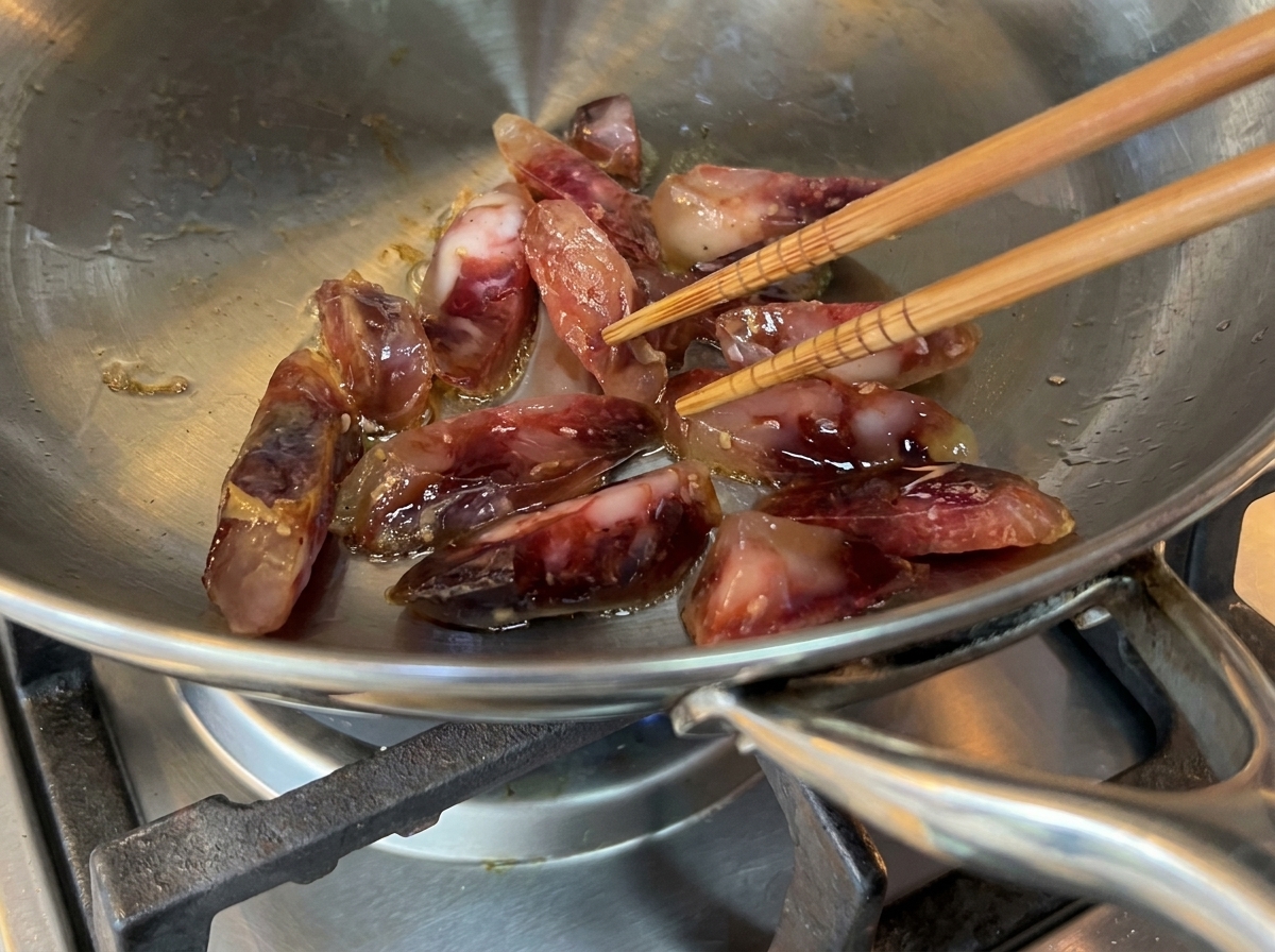 Trozos de embutido chisporroteando en una sartén de acero inoxidable con aceite de oliva.