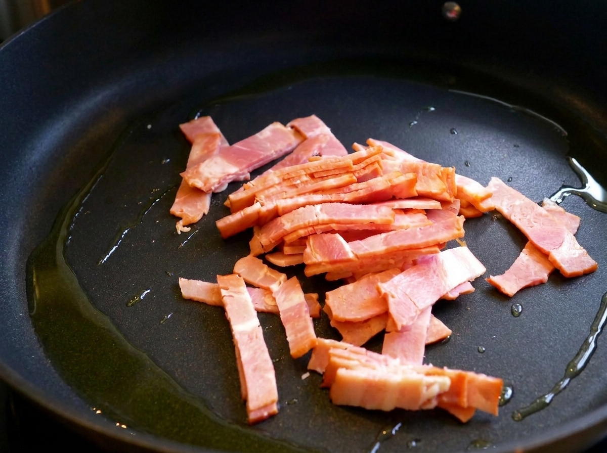 Tiras de beicon friéndose en una sartén con un chorrito de aceite de oliva.