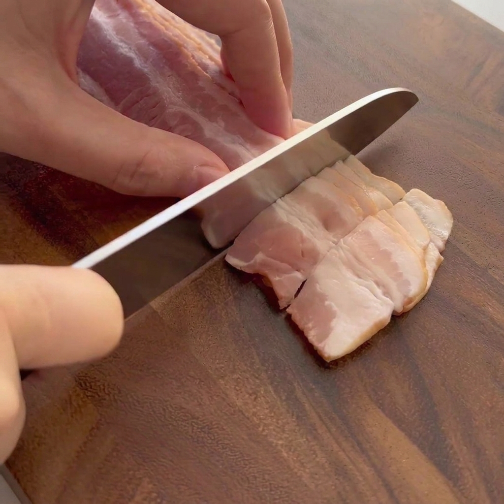 Tiras de tocino crudo siendo cortadas sobre una tabla de madera.