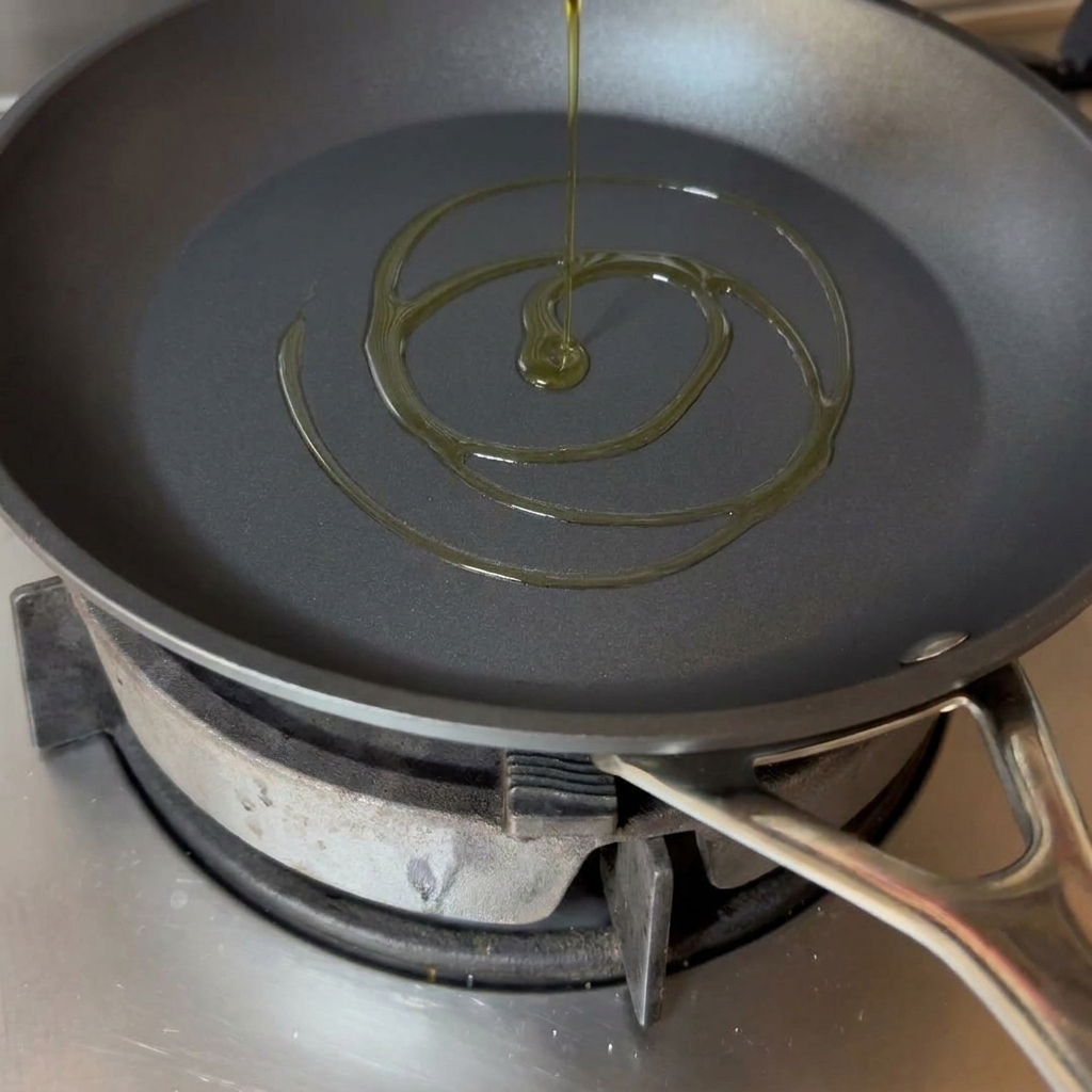 Un chorro de aceite de oliva dorado asentándose en el fondo de una sartén negra.