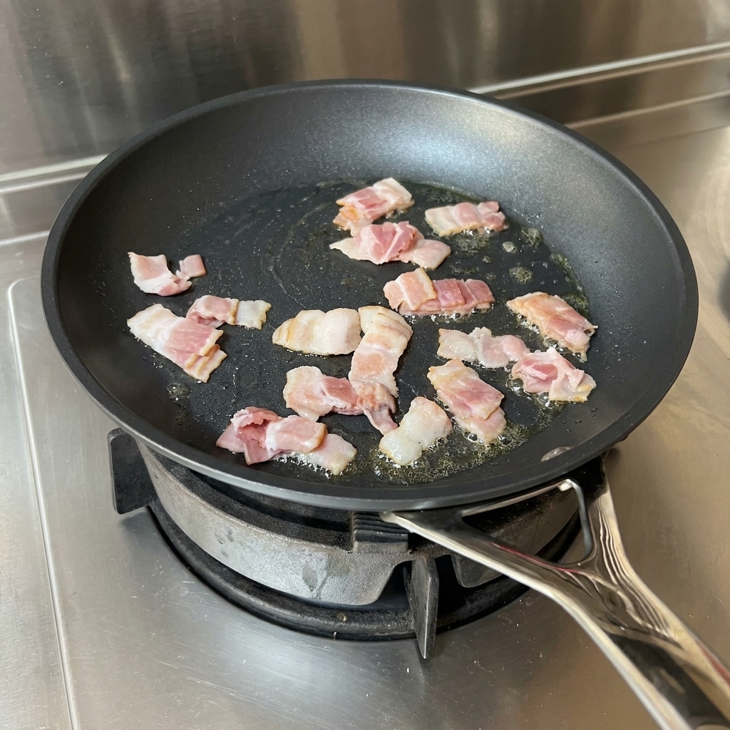 Tiras de tocino friéndose en aceite, siendo removidas por una espátula roja.