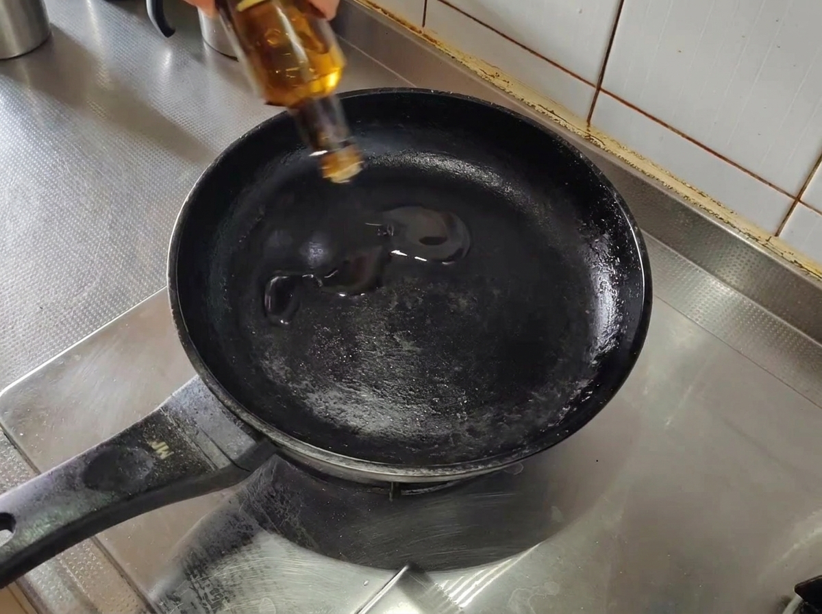 Aceite de oliva siendo vertido en una sartén negra precalentada en la cocina.