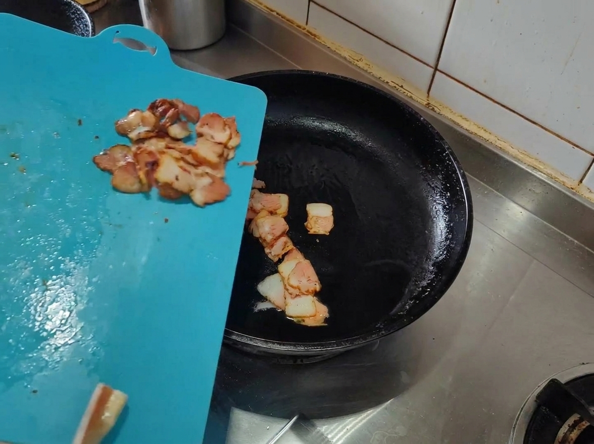 Tiras de bacon crudo siendo añadidas a una sartén caliente con aceite de oliva.
