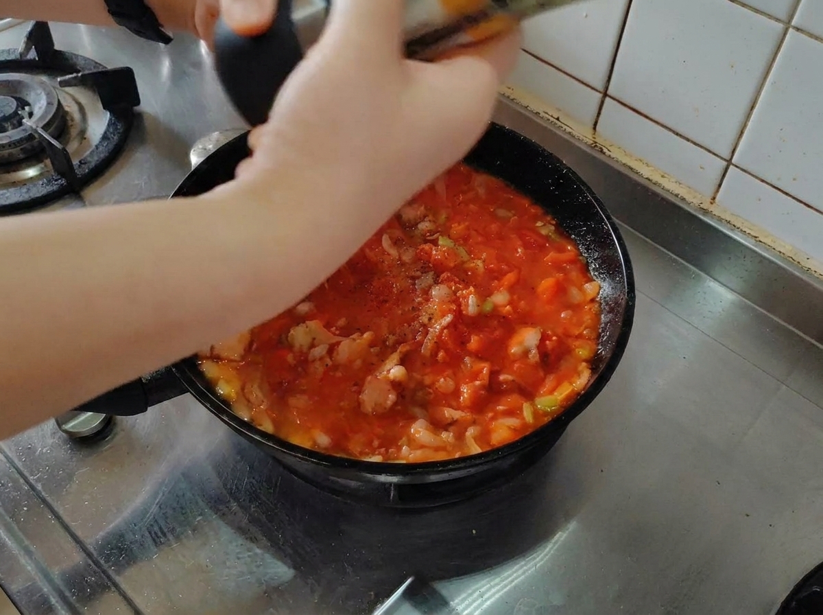 Pimienta negra recién molida sobre una salsa de tomate y bacon que hierve a fuego lento en una sartén negra.