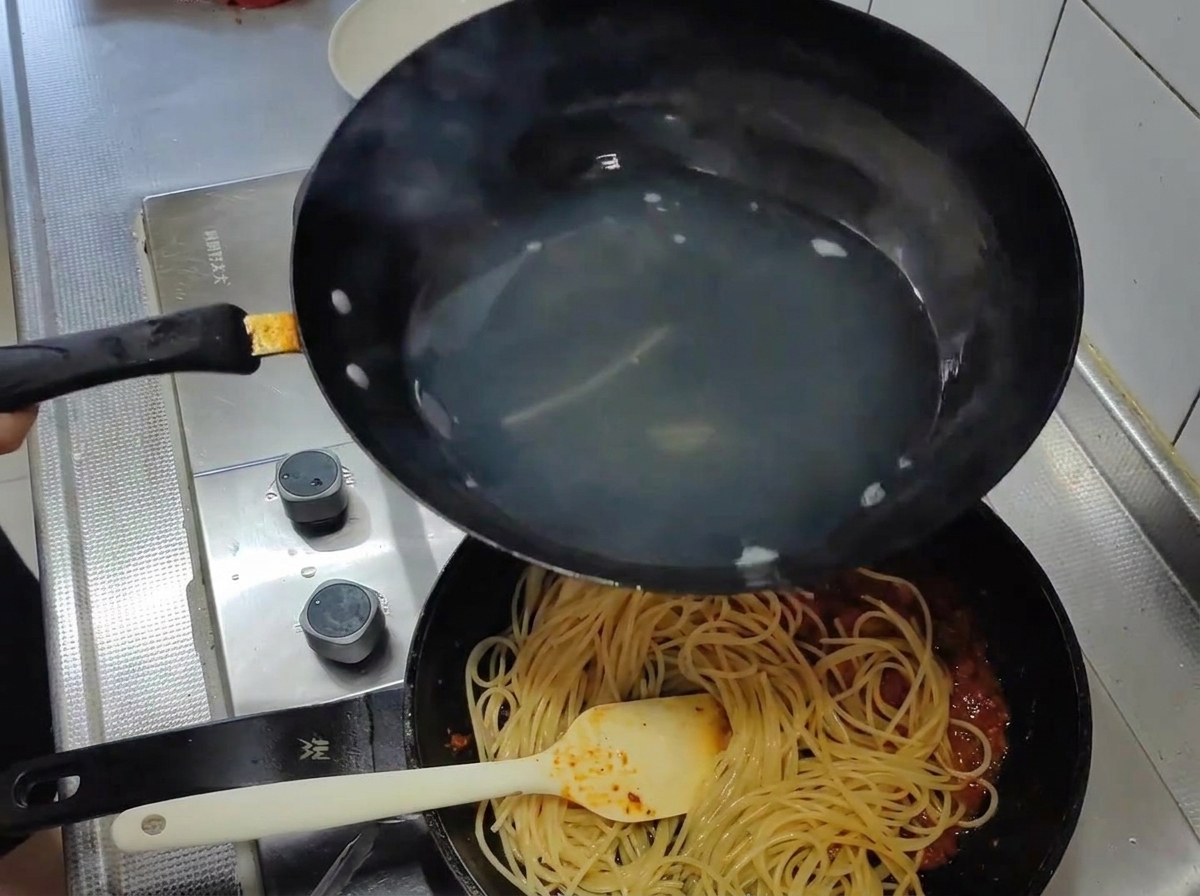Espaguetis cocidos siendo trasladados desde el agua hirviendo a una sartén con salsa de tomate roja y rica.