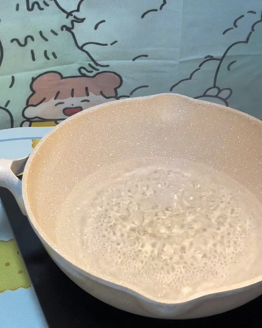 Hebras de pasta seca siendo colocadas con cuidado en una olla de agua hirviendo.
