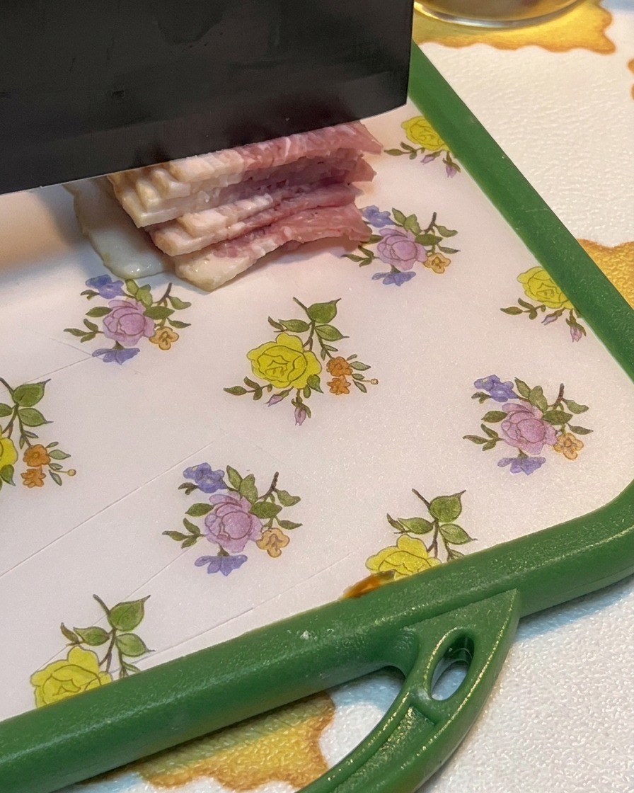 Tiras de tocino crudo siendo cortadas en trozos pequeños sobre una tabla de cortar.