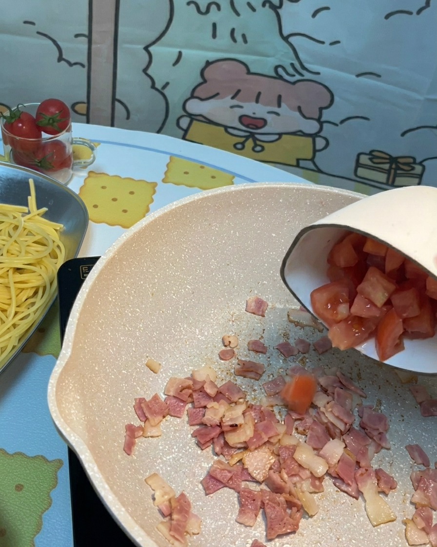 Tomates frescos picados añadidos a la sartén con trozos de tocino crujiente.