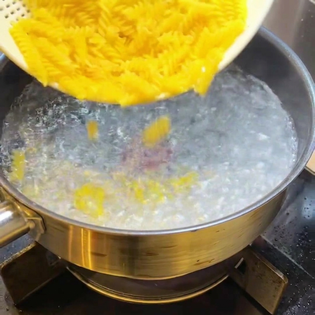 Pasta fusilli seca siendo añadida a una olla con agua hirviendo.