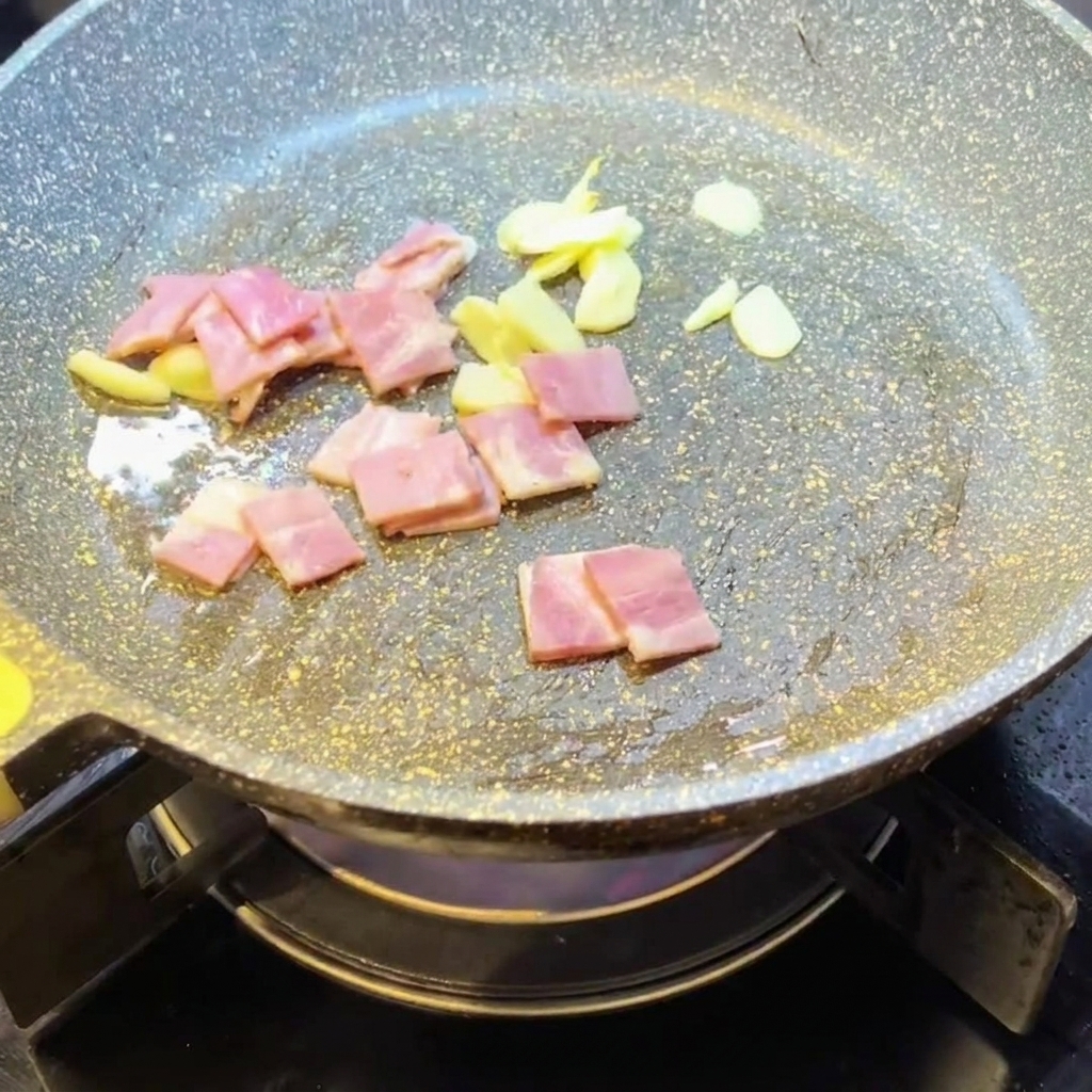 Trozos de beicon picado friéndose en una sartén con ajo.