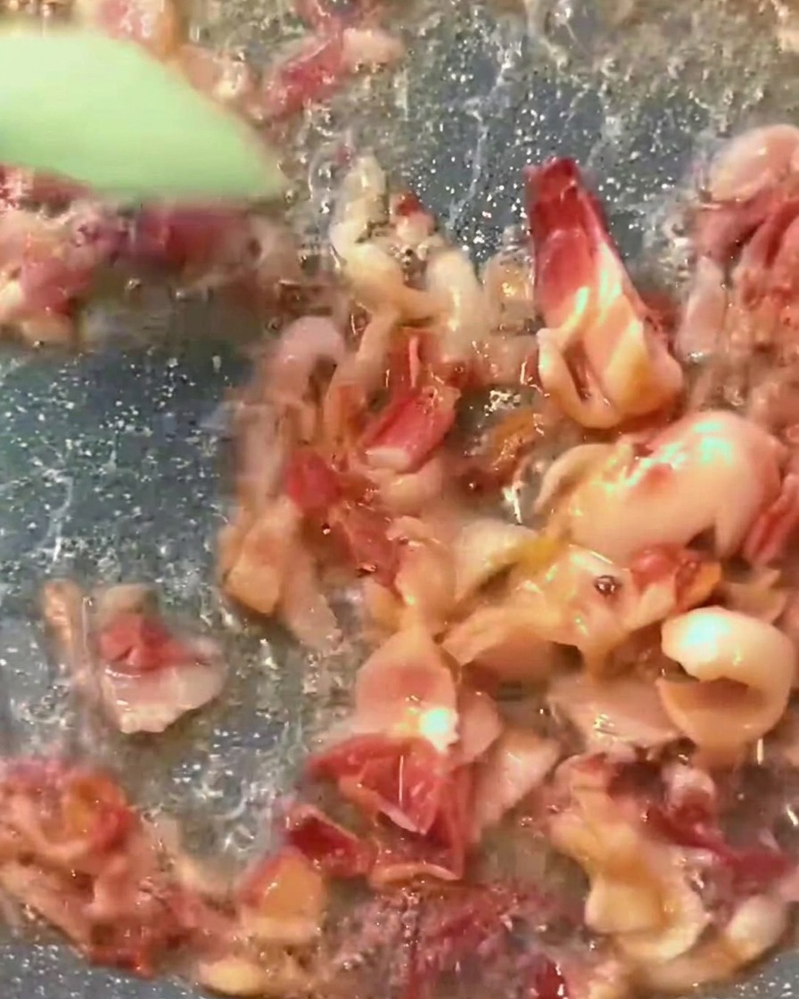 Rica salsa de tomate roja burbujeando en una sartén con trocitos de tocino dorados mezclados.