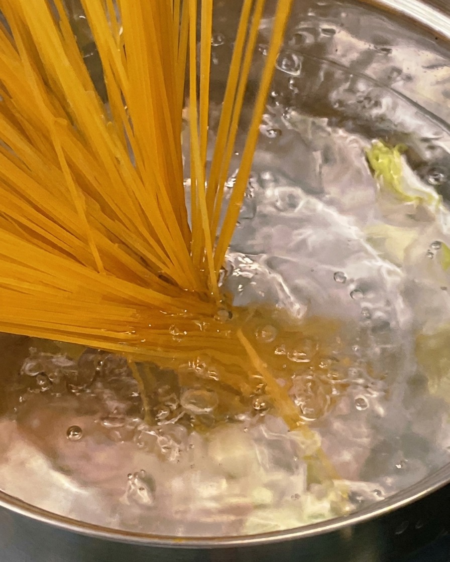Una cuchara de madera removiendo una salsa espesa y sabrosa de tomate y tocino en una sartén de acero inoxidable.