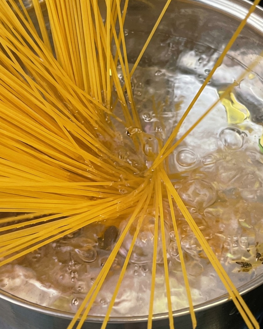 Pasta al dente siendo sacada de una olla con un servidor de pasta dentado, con vapor elevándose por encima de la olla.