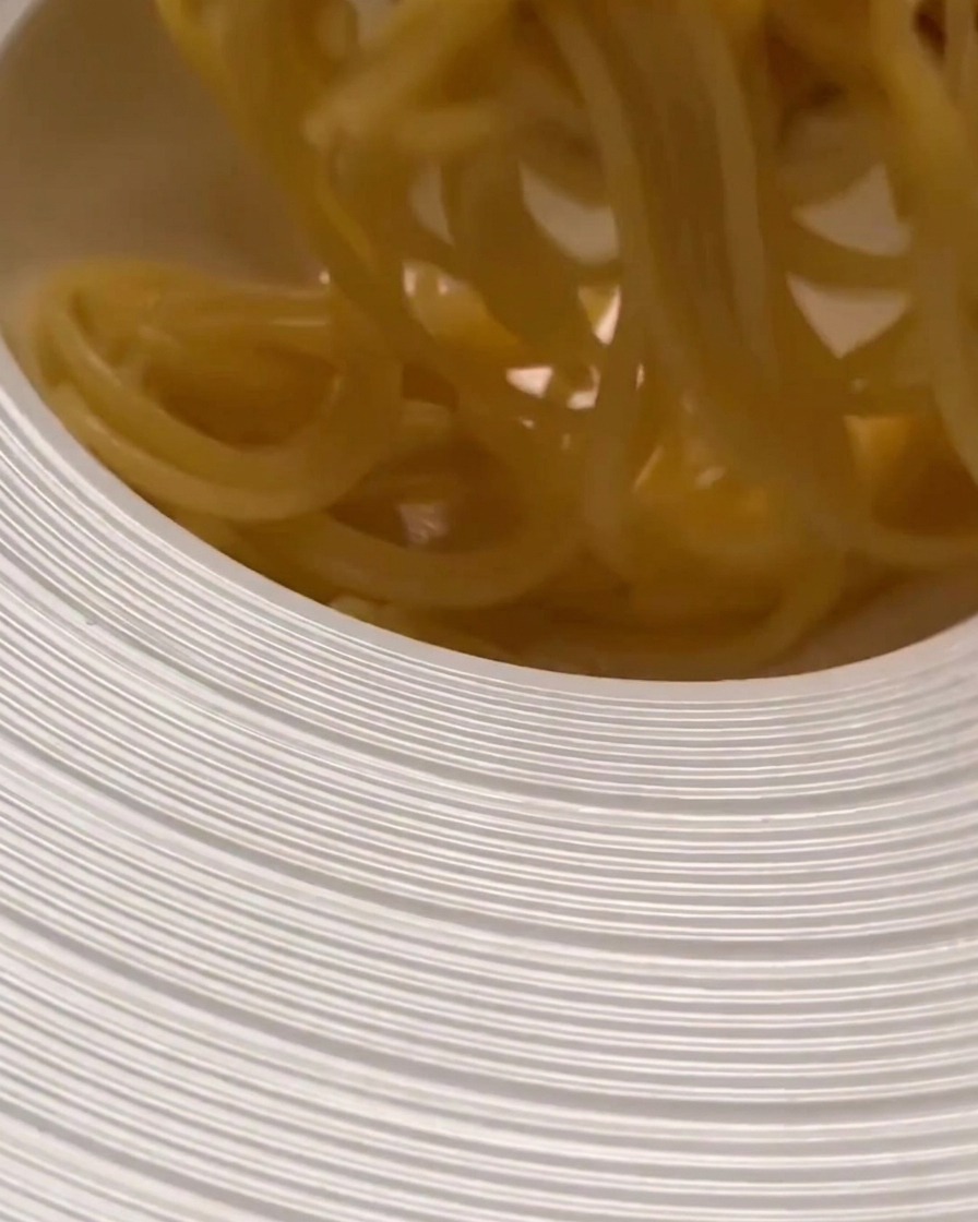 Pasta cocida siendo transferida a un tazón ancho para servir, lista para ser mezclada con la salsa.