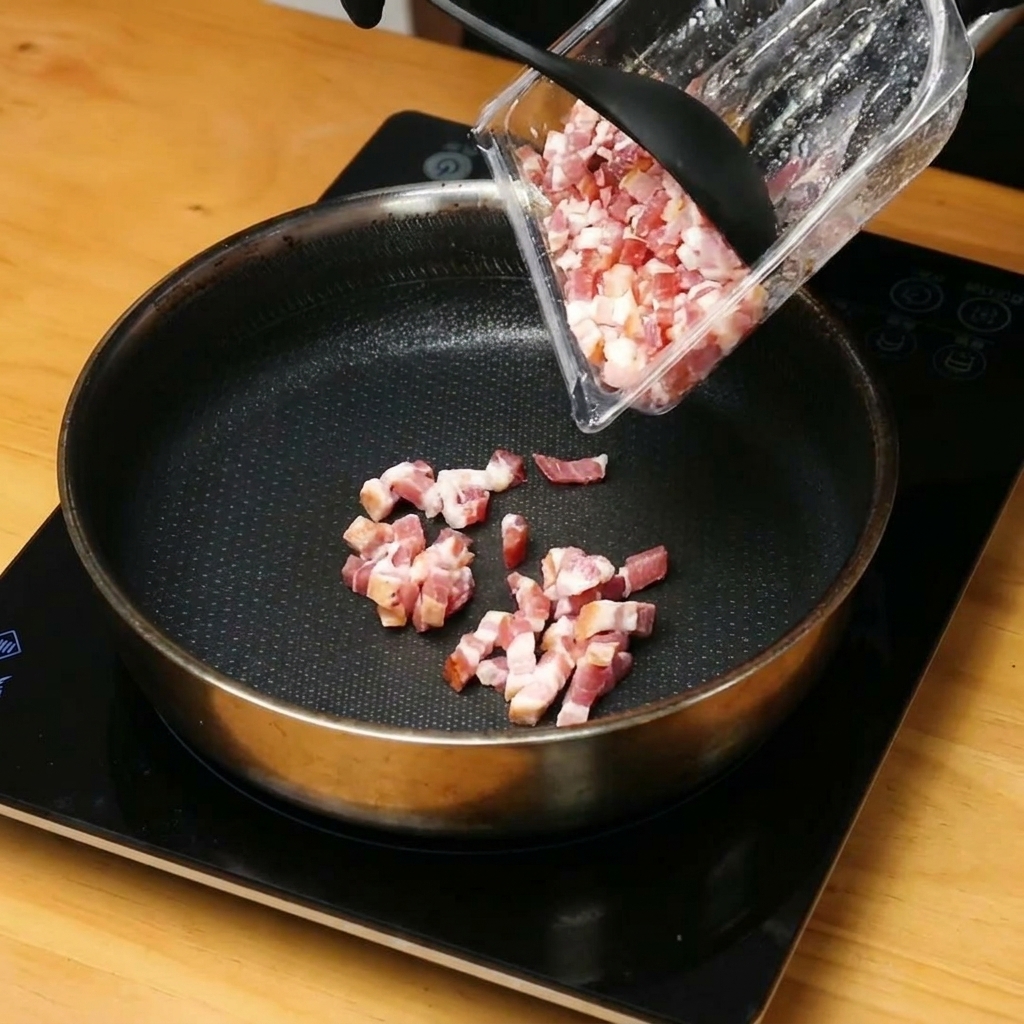 Trozos de bacon picado dorándose y soltando grasa en una sartén caliente.