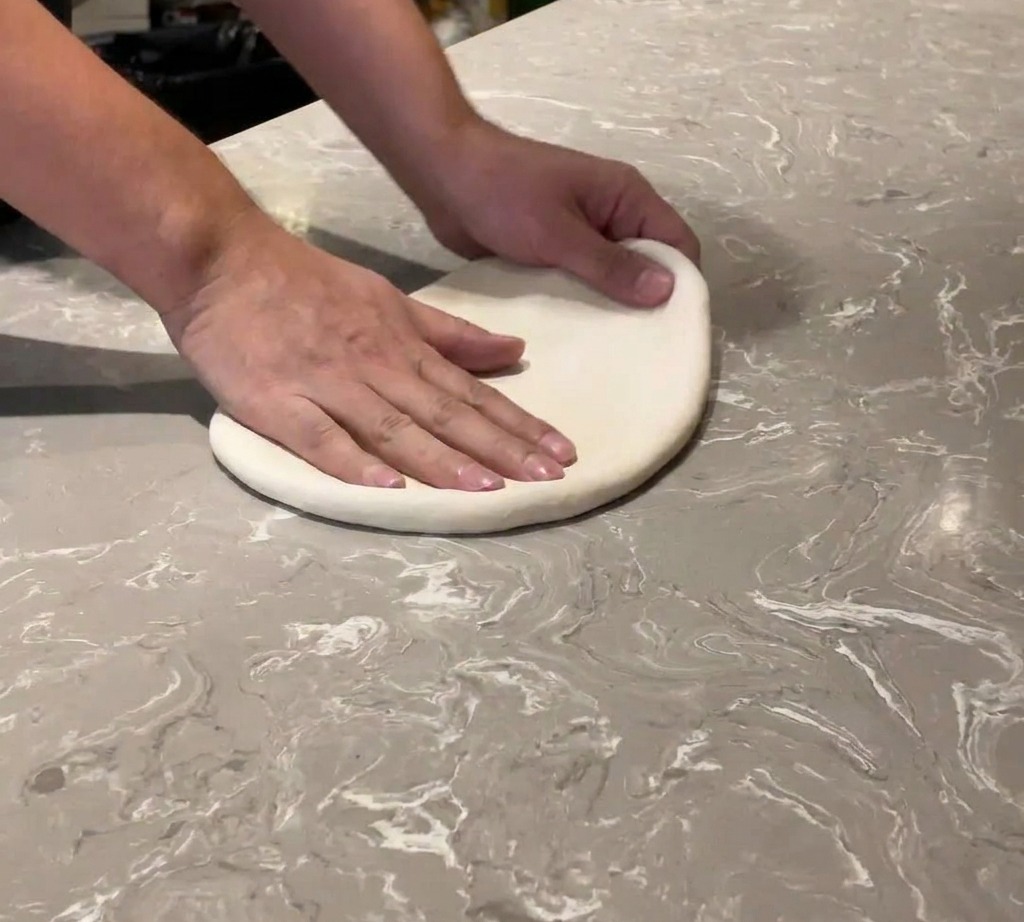 Primer plano de unas manos estirando una bola de masa suave sobre una superficie de mármol.