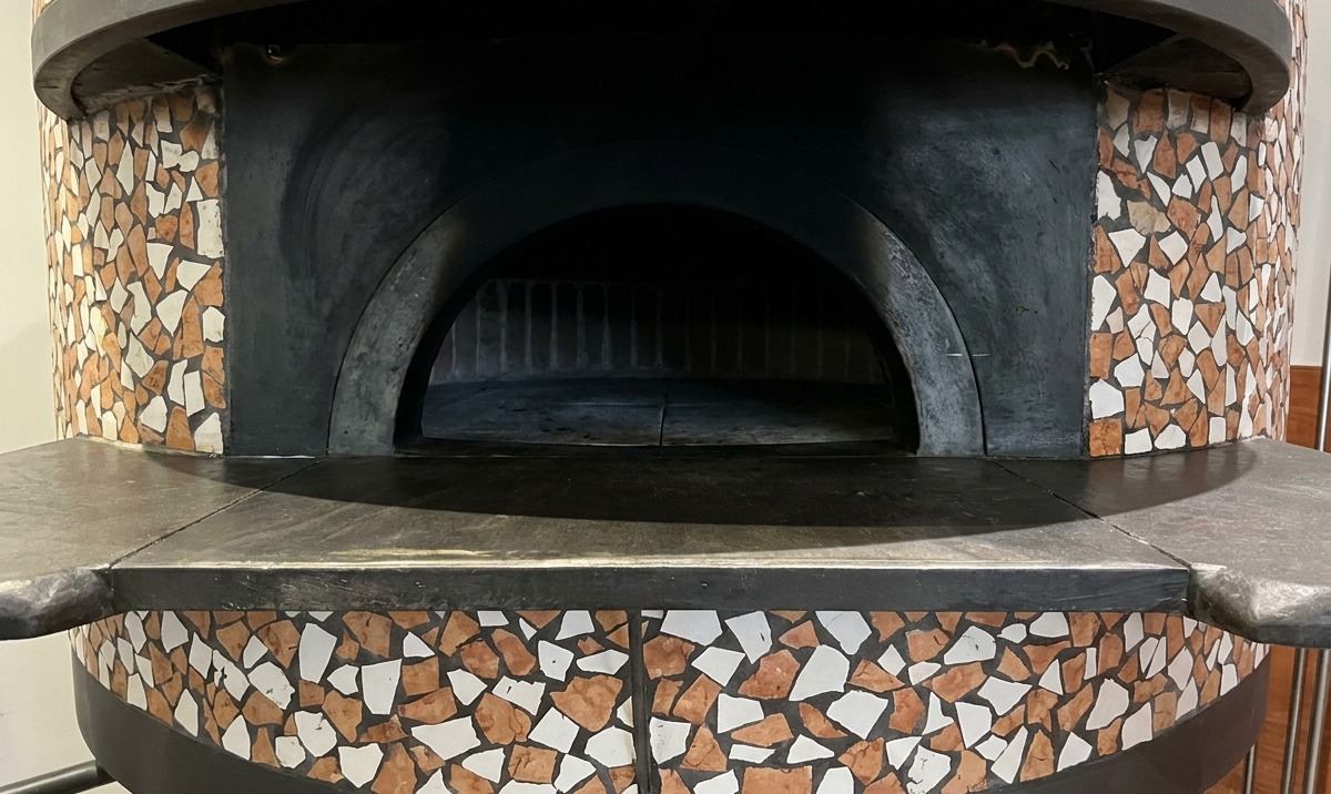 Una pizza horneándose dentro de un horno de leña, con los bordes burbujeando y tostándose junto al fuego.