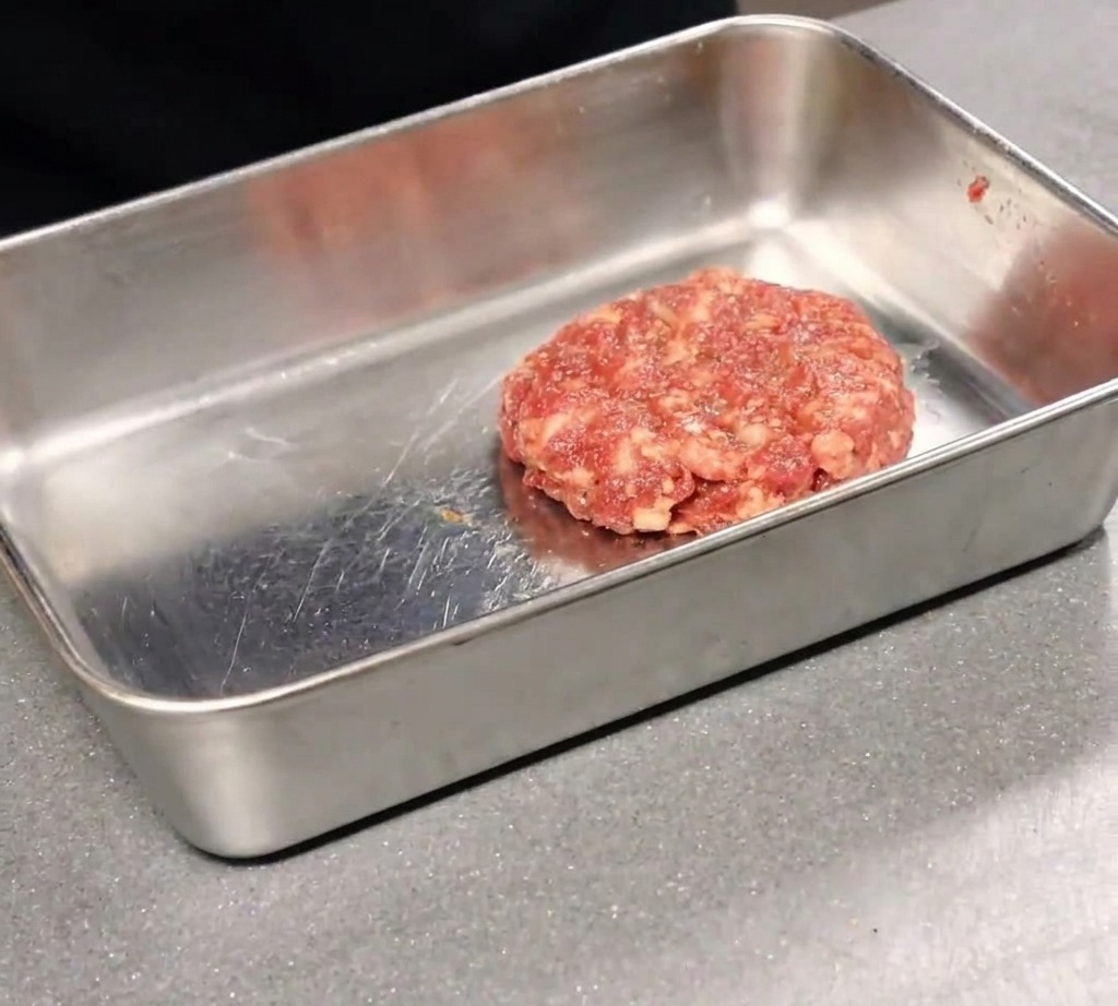 Una pizza recién hecha, cortándose en porciones con un cortapizzas sobre una tabla de madera.
